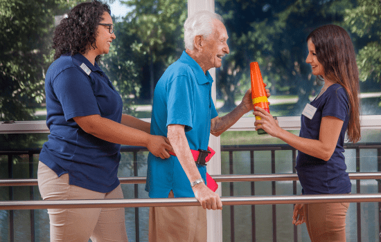 Healthcare workers assist an elderly man with physical therapy exercises.