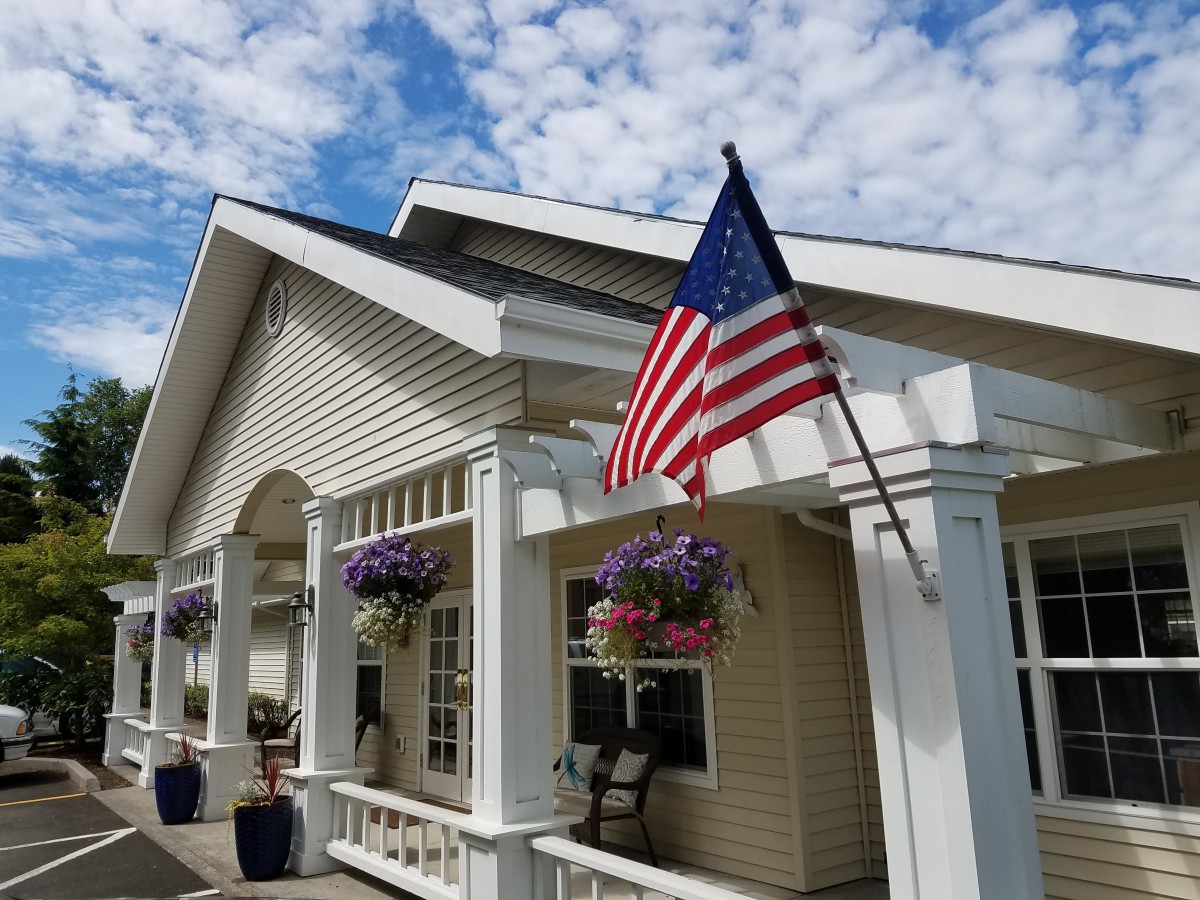 A suburban house with a porch, displaying the American flag and decorated with hanging plants.