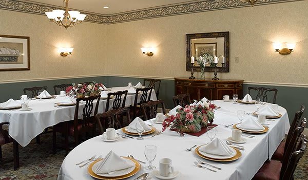 A formal dining room with elegantly set tables and flower centerpieces.