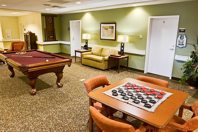 A cozy game room featuring a billiards table and a checkers board on a table, with comfortable seating for relaxation.