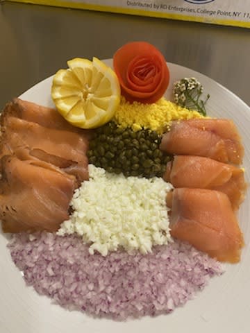 A beautifully arranged platter of smoked salmon with garnishes including lemon, capers, diced onion, and egg yolk.