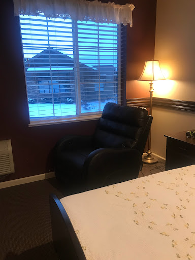 A cozy bedroom setting featuring a recliner chair, lamp, and a view out the window.