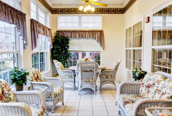 A cozy sunroom with wicker furniture and a dining table, surrounded by large windows and adorned with curtains.