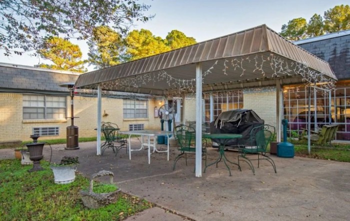A backyard patio area with an awning, featuring outdoor furniture including chairs and a table.