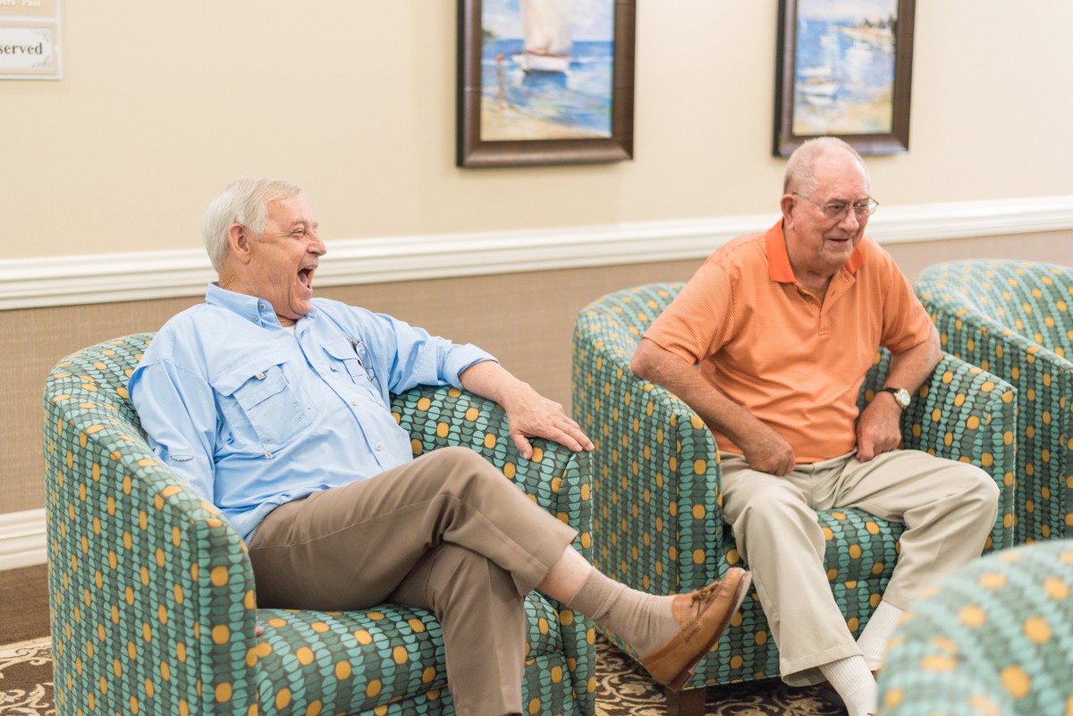 Two elderly men enjoying a conversation and laughing in a comfortable indoor setting.