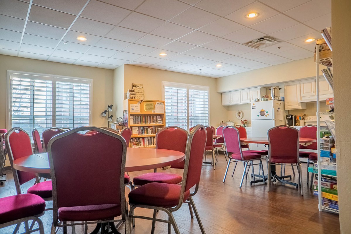 A community room with tables, chairs, and a kitchen area.