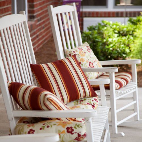 A cozy porch setting with white rocking chairs adorned with striped and floral cushions.