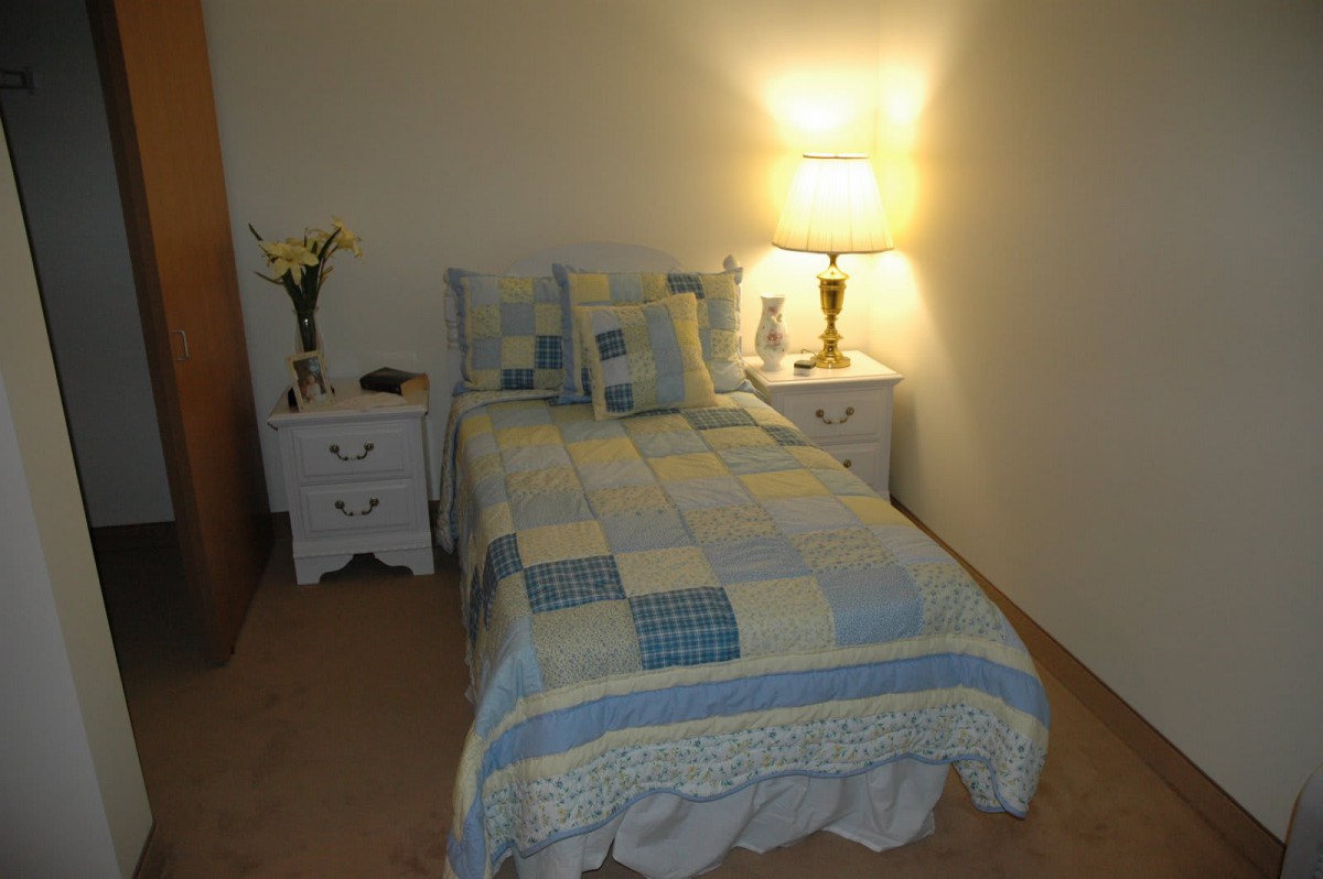 A cozy bedroom with a quilted bedspread and a warmly lit lamp on the nightstand.