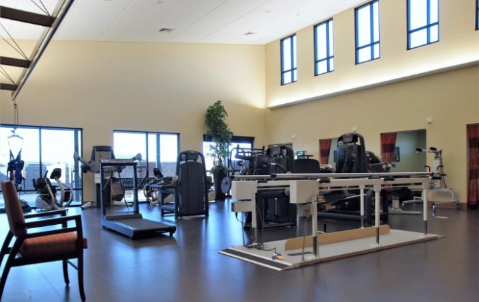 A spacious gym with various exercise equipment and bright natural lighting.