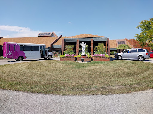 A view of a facility featuring transportation vehicles parked outside, with a landscaped area and a statue.
