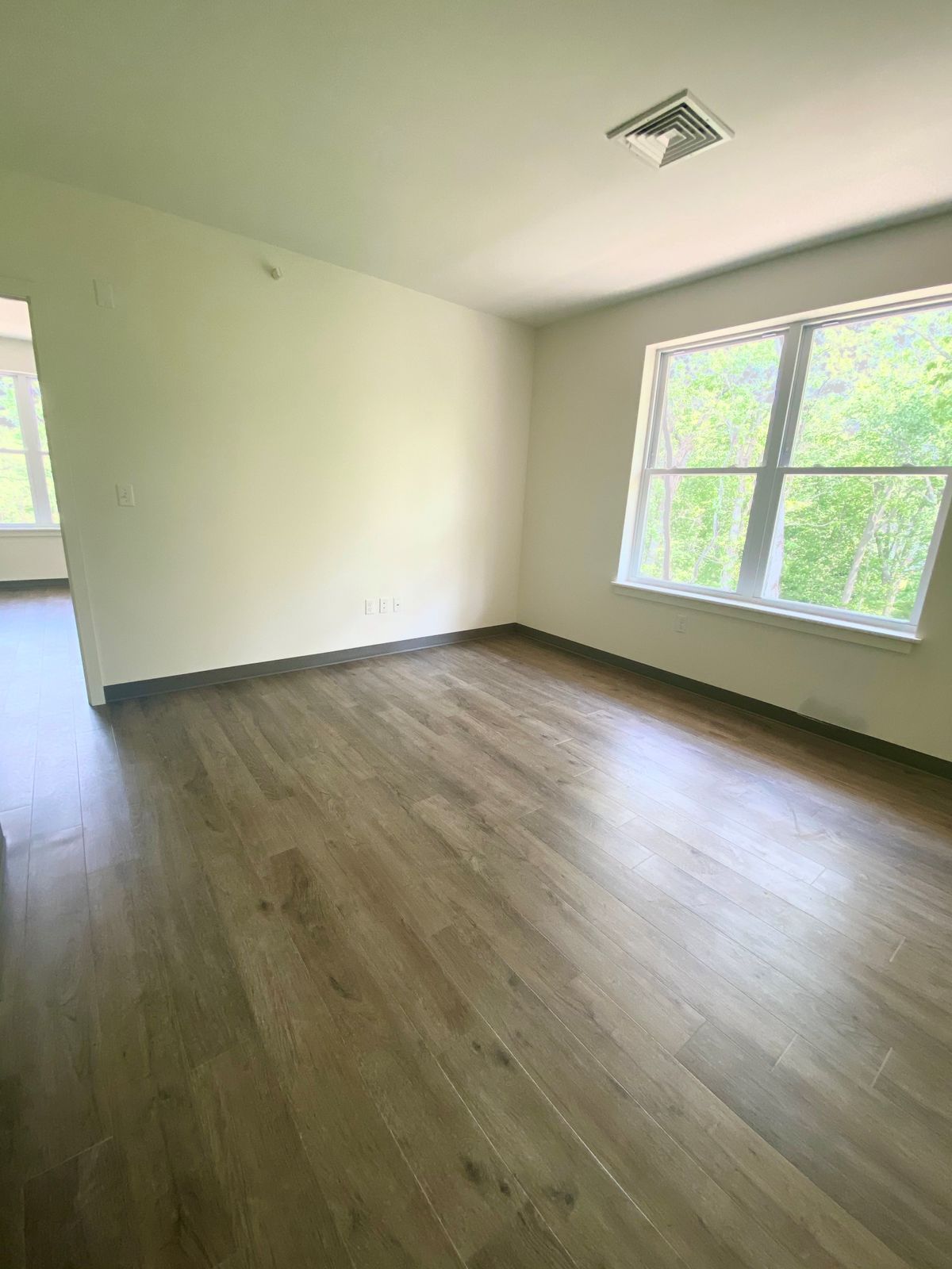 An empty room with hardwood flooring and a large window letting in natural light.