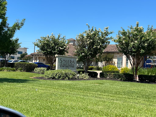 A well-maintained residential community sign surrounded by lush greenery and a clear blue sky.