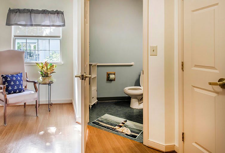 A view of a bathroom through an open door, featuring a toilet and a window with natural light.