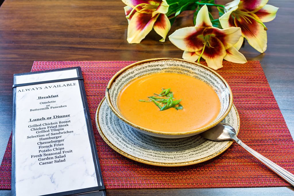 A bowl of soup served on a table with a menu and flowers.
