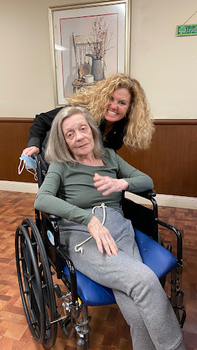 A joyful moment shared between a caregiver and an elderly woman in a wheelchair.