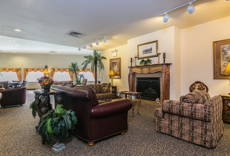A cozy living room with a fireplace, leather sofa, and plaid armchair surrounded by houseplants.