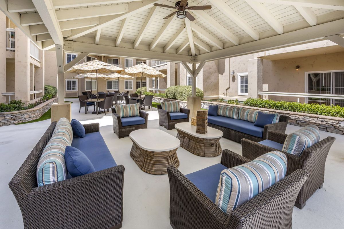 A stylish outdoor patio area with wicker seating, cushioned sofas, and a pergola with a ceiling fan.