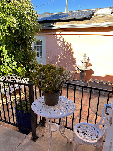 A serene outdoor balcony with a potted plant and a fountain in the background, basking in the sunlight.