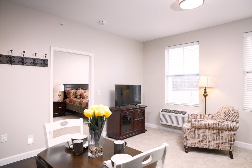 A cozy living room with a dining area, featuring a television, table with flowers, and comfortable seating.