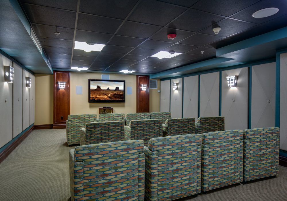 A modern waiting room with rows of comfortable seating facing a large television.