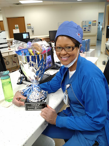 A dedicated nurse proudly holds a trophy in a hospital setting, celebrating her achievements.