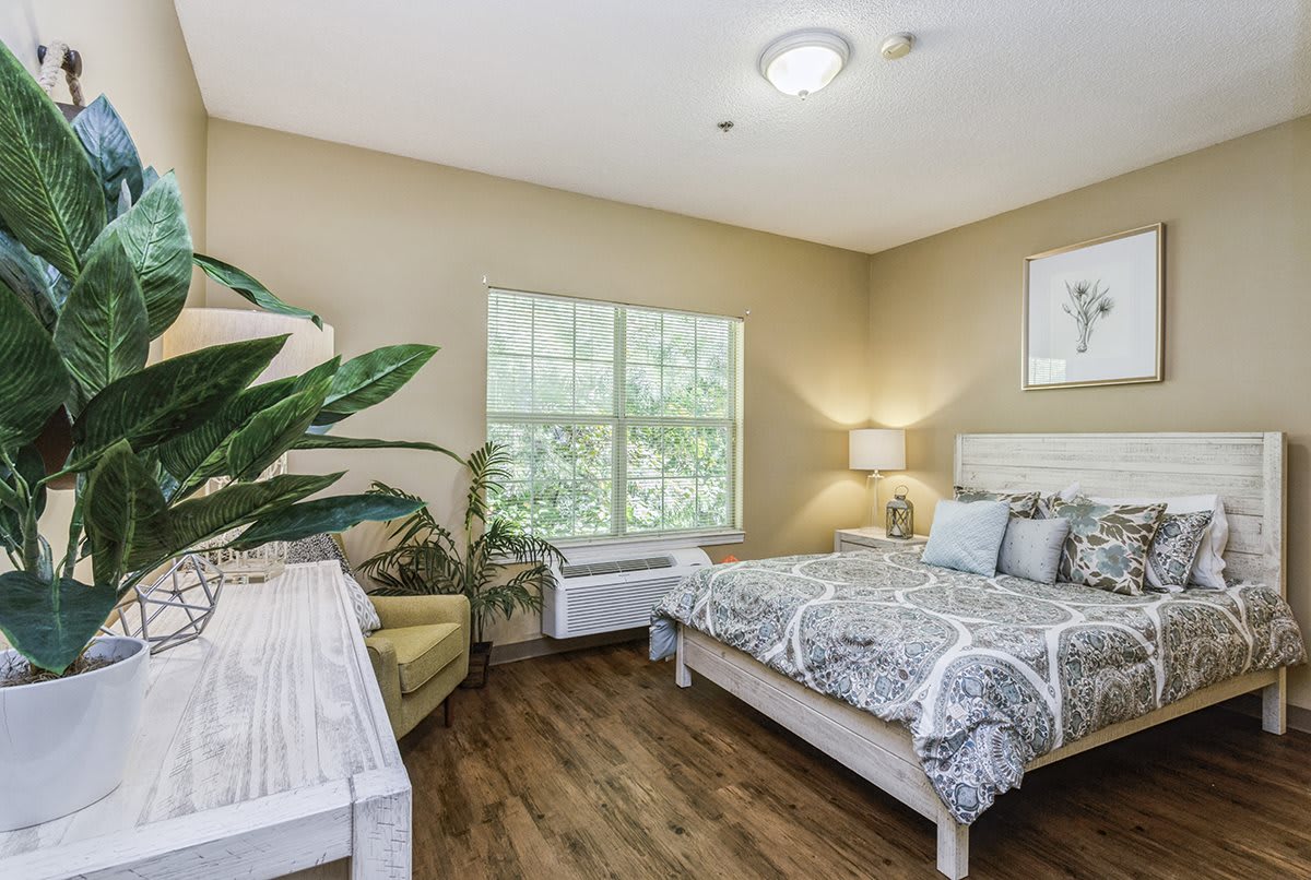 A cozy bedroom with a bed, desk, chair, and potted plant near the window.