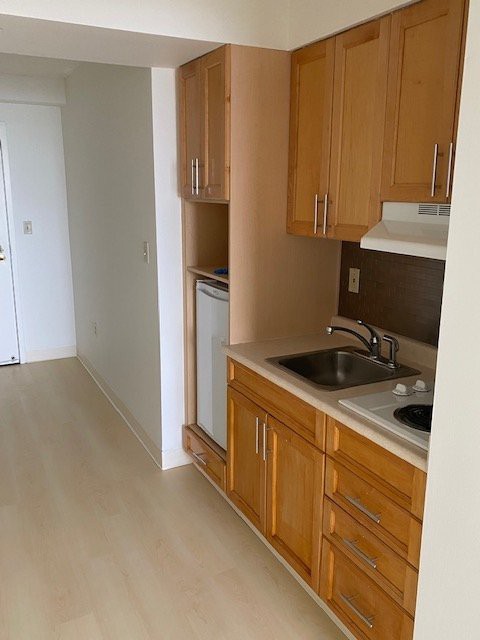 A compact kitchen with wooden cabinets, featuring a sink, refrigerator, electric stove, and vent hood.