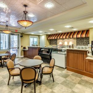 A cozy cafeteria with round tables and a buffet area, featuring warm lighting and inviting decor.