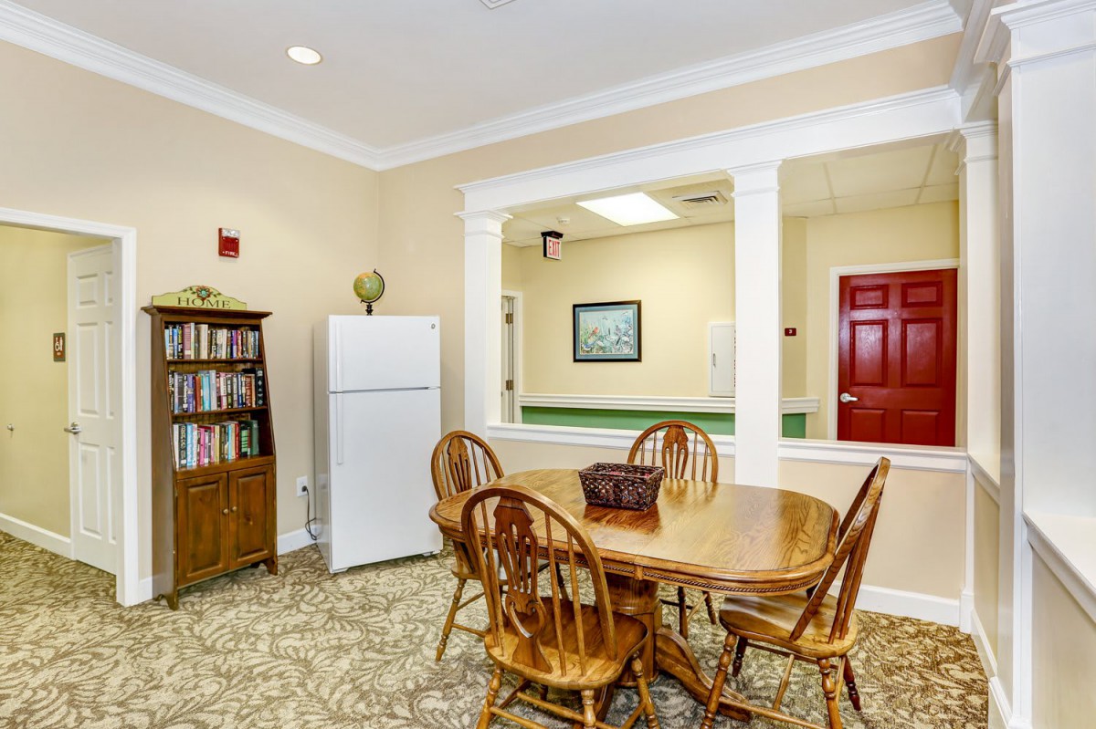 A cozy dining area with a wooden table and chairs, a bookshelf, and a refrigerator.
