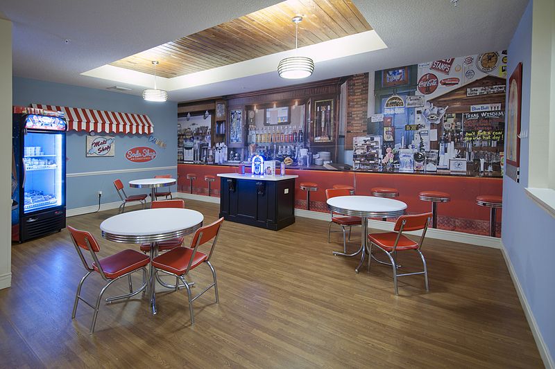 A retro-themed diner interior with round tables and red chairs, featuring vintage wall decor.