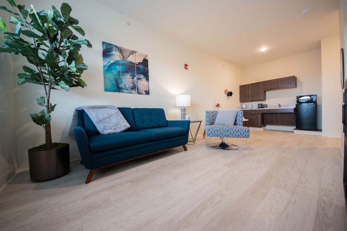 A modern living room with a blue sofa, armchair, and a kitchen area in the background.