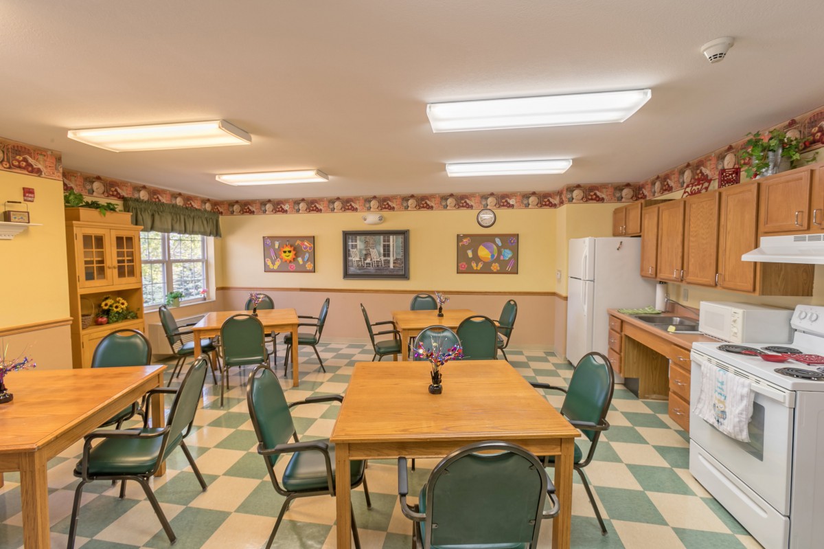 A communal dining room with several tables and chairs, featuring a checkered floor and wall-mounted artwork.