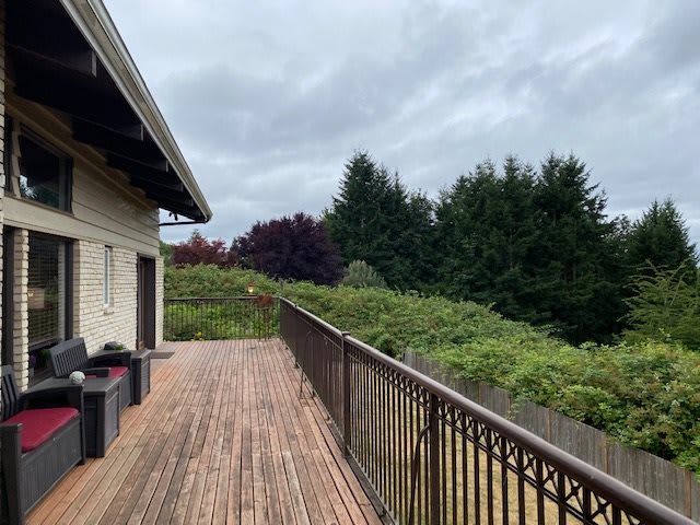 A spacious wooden deck with a view of lush greenery and a cloudy sky.