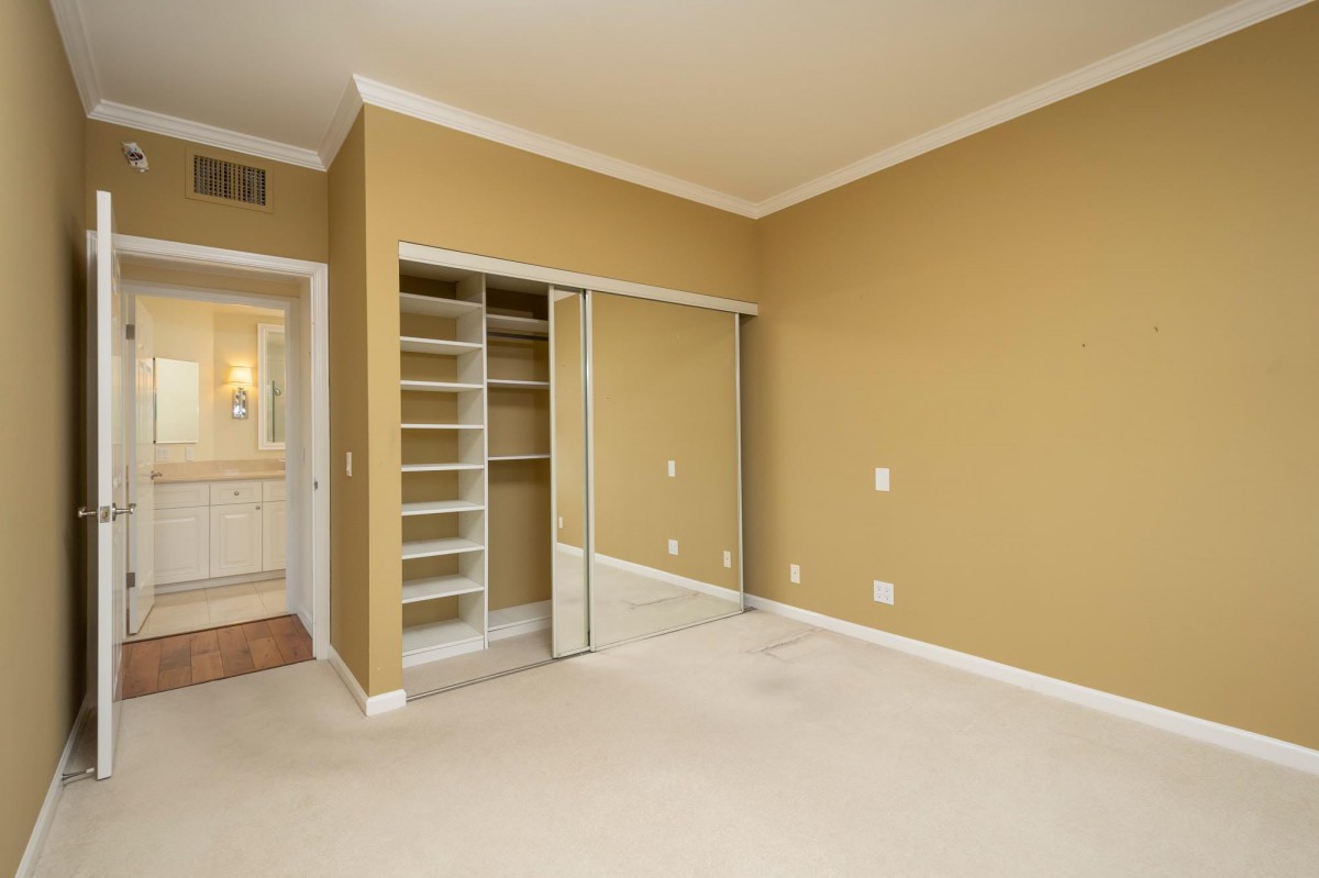 An empty room with beige walls, carpeted flooring, and mirrored sliding closet doors.