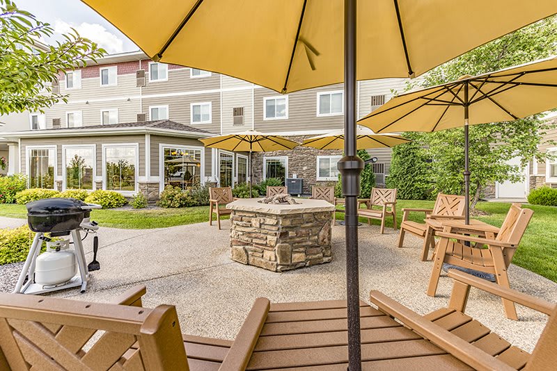 A cozy outdoor patio with yellow umbrellas, wooden chairs, and a central stone fire pit.