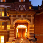 A warmly lit entrance to a grand brick building during the evening.