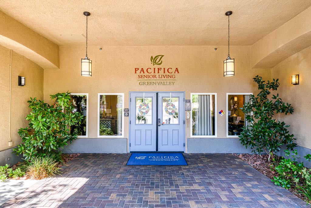 The main entrance of Pacifica Senior Living, featuring blue double doors and surrounding plants.