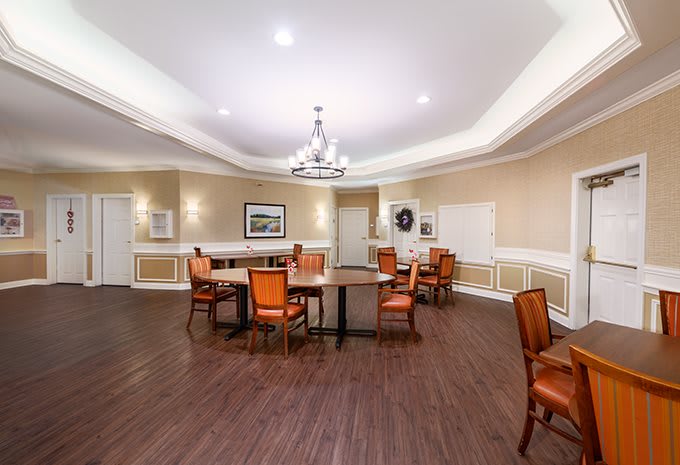 A spacious dining area with wooden flooring, featuring tables and chairs arranged neatly under elegant lighting.