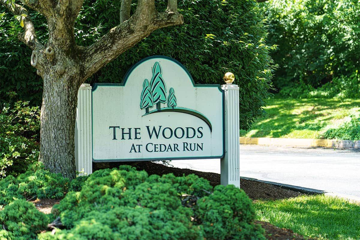 Sign for 'The Woods at Cedar Run' surrounded by trees and landscaping.