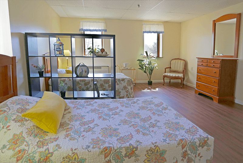 A bright and spacious bedroom with a floral bedspread, decorative plants, and elegant furniture.