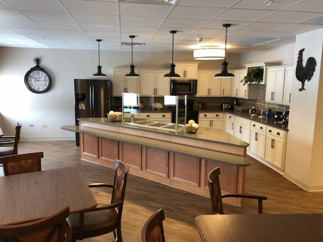 A modern kitchen with an island and pendant lighting, featuring wooden floors and nearby dining area.