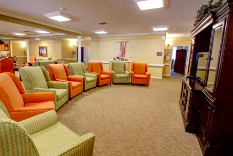 A spacious room with a circular arrangement of green and orange chairs, featuring a carpeted floor and soft lighting.