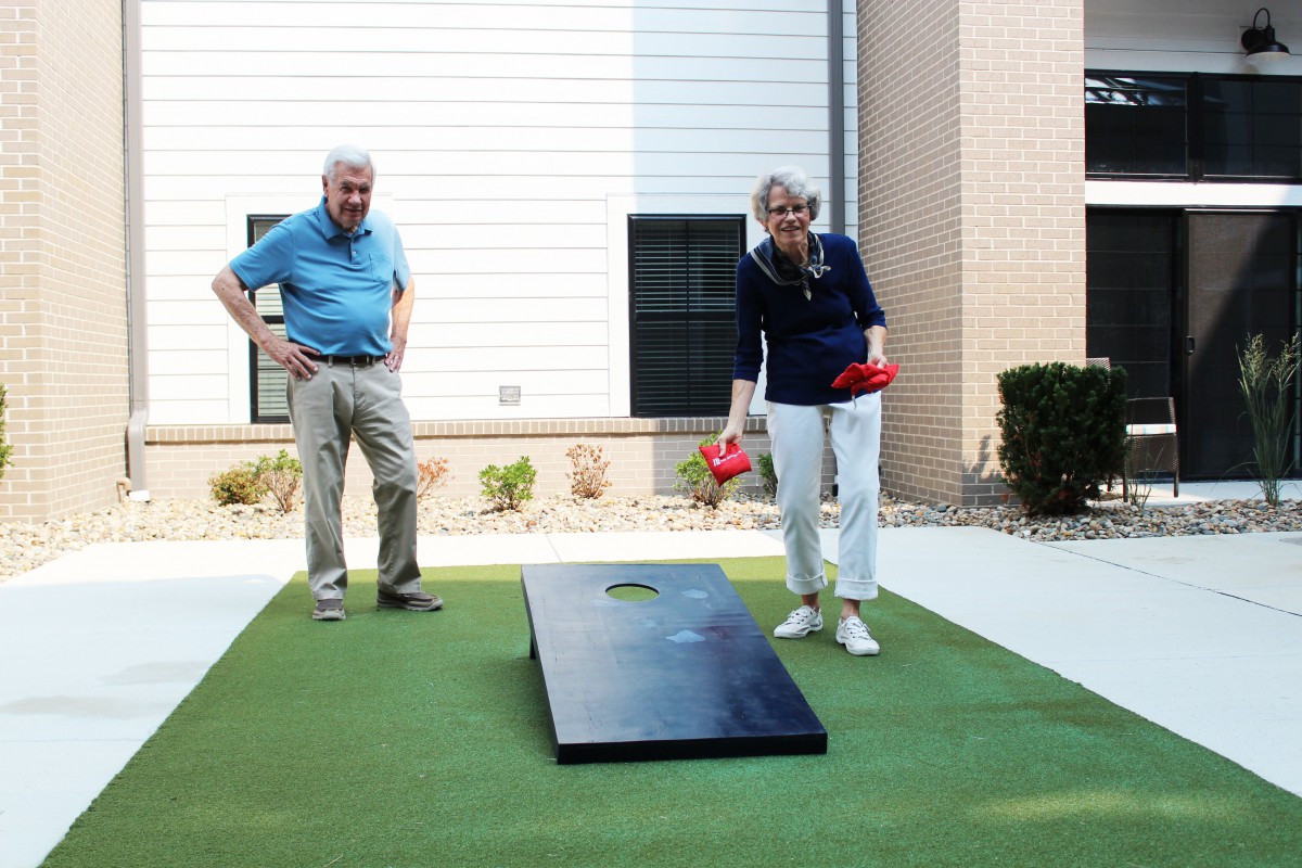 An elderly couple enjoys playing a game of cornhole outside on a sunny day.