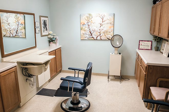 A well-organized hair salon room with a styling chair, mirror, artwork on the wall, and salon equipment.