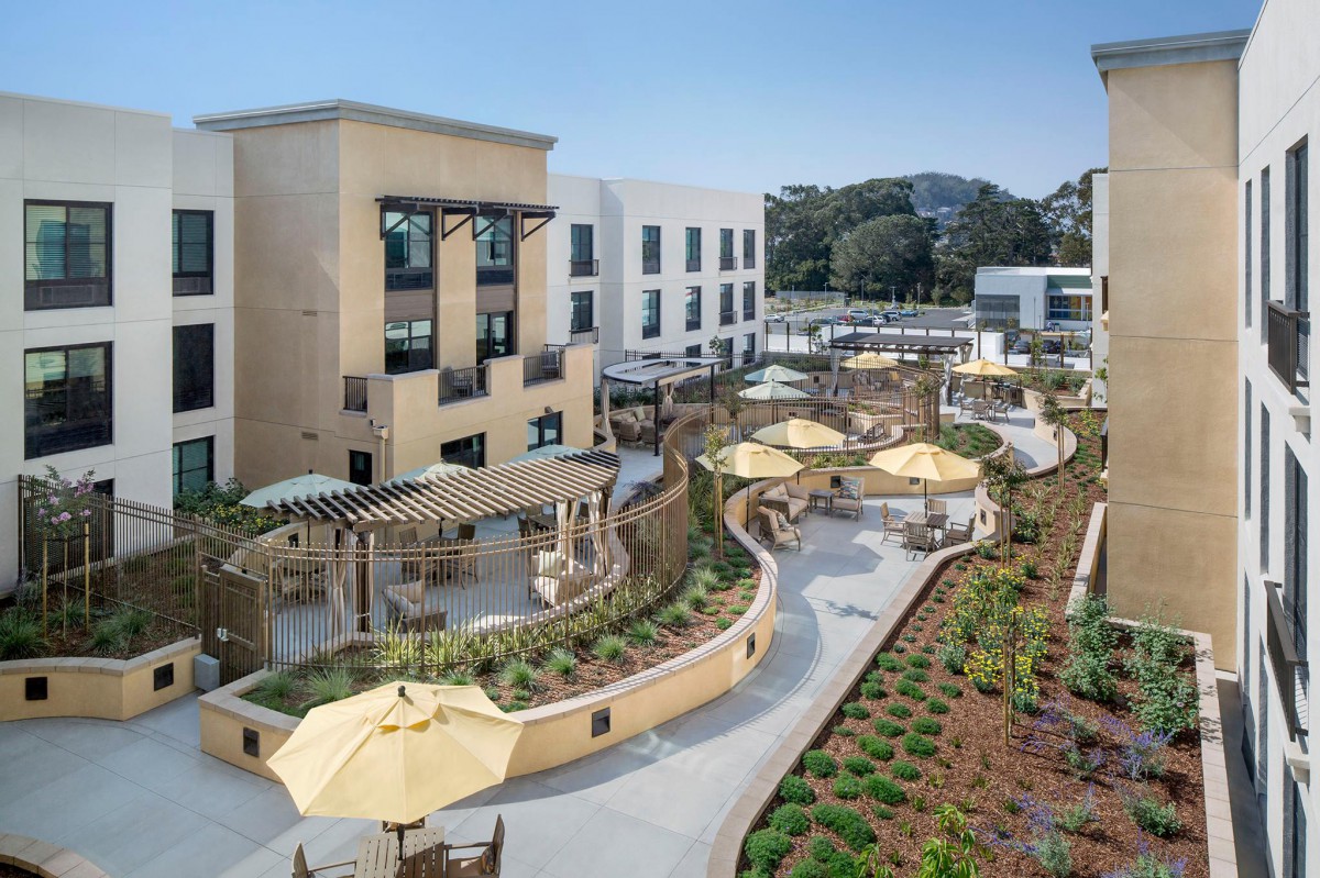 A view of a hotel with a spacious outdoor patio featuring umbrellas and landscaped gardens.