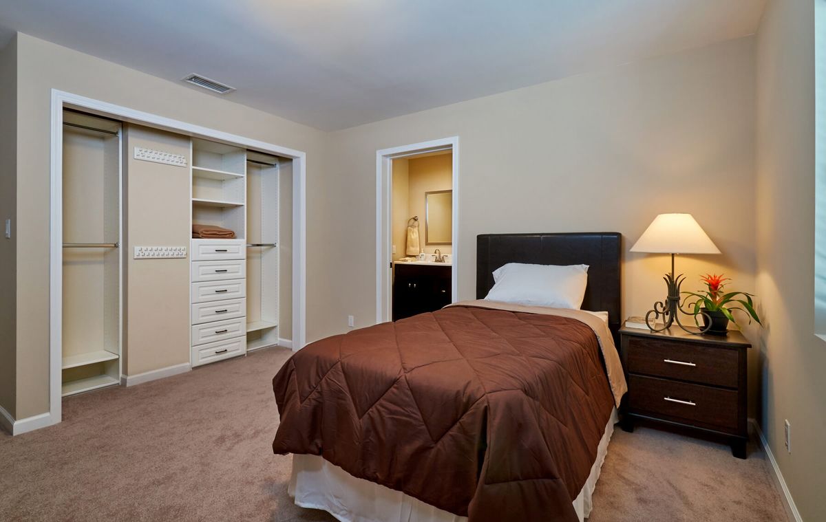 A cozy bedroom with a single bed, open closet, and warm lighting.