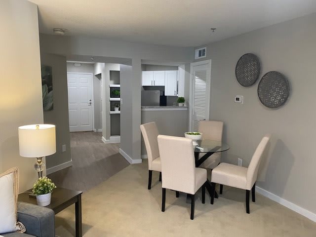 A modern dining area with a glass table and upholstered chairs in an apartment setting.
