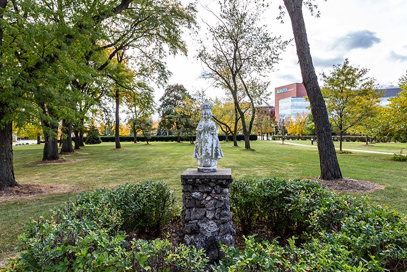 A serene statue stands amidst lush greenery in a tranquil park setting.