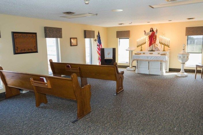 A small chapel interior featuring wooden pews, an altar, and a religious statue.
