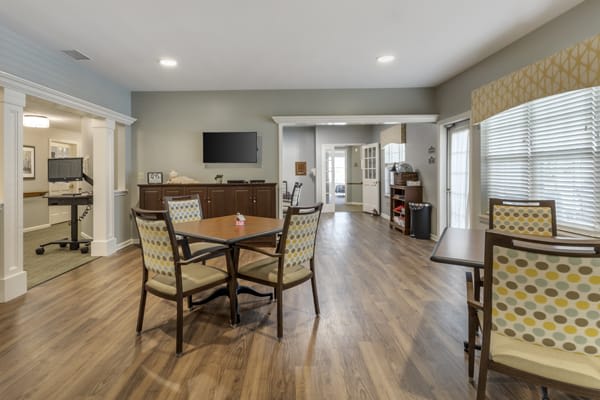 A modern living room and dining area with wood flooring, featuring a table, chairs, and a wall-mounted TV.